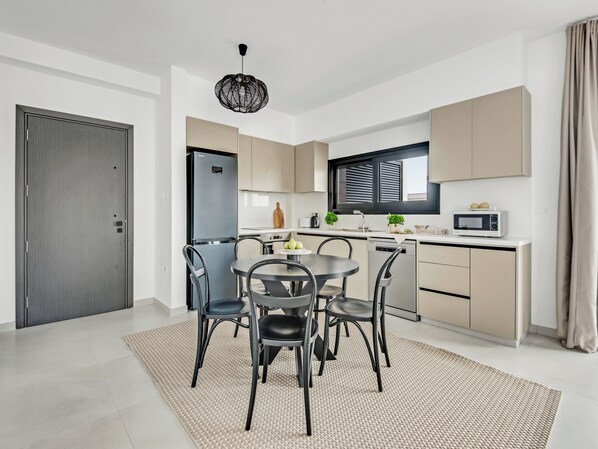A modern kitchen with a dining area, featuring a built-in oven, microwave, and a dining table with chairs. - Sanders Only Limassol - Full Building (Limassol)