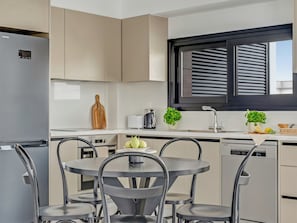 A modern kitchen with a refrigerator, a sink, a window with blinds, and a dining area with chairs and a table. - Sanders Only Limassol - Full Building (Limassol)