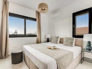 A modern hotel room with a large bed, two bedside tables, a window with a view, and a hanging light fixture. - Sanders Only Limassol - Full Building (Limassol)