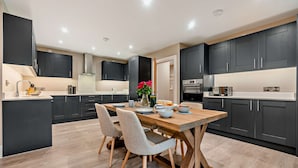 A modern kitchen with dark cabinets, a wooden dining table, and a central island with seating.