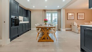A modern kitchen with dark cabinets, a wooden dining table, and a view through a glass door.