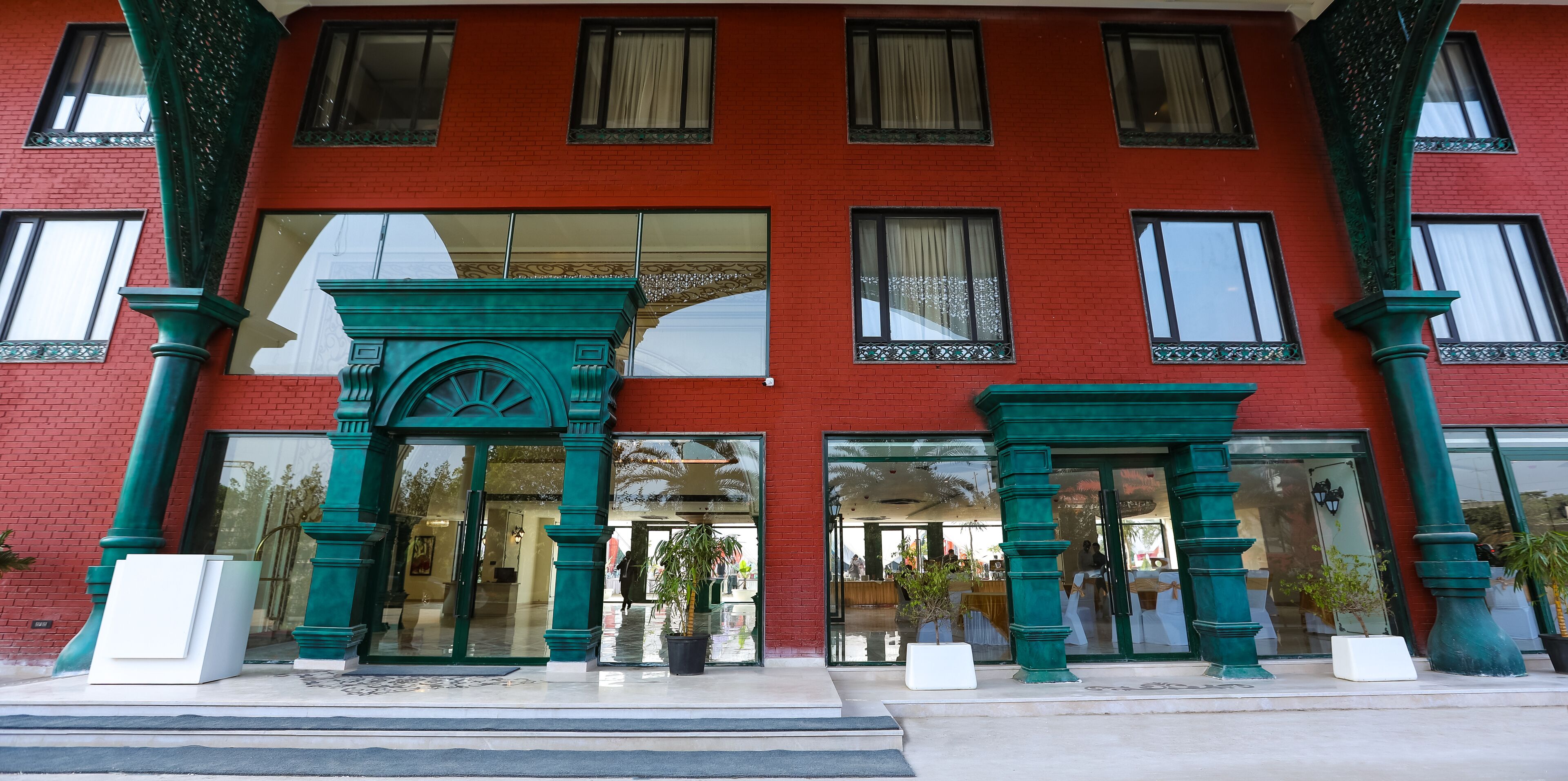 A red brick building with green decorative columns and large glass doors.