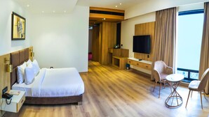 A hotel room with a bed, bedside table, lamp, TV, and a seating area with chairs and a table. - DAYAL GATEWAY (Lucknow)