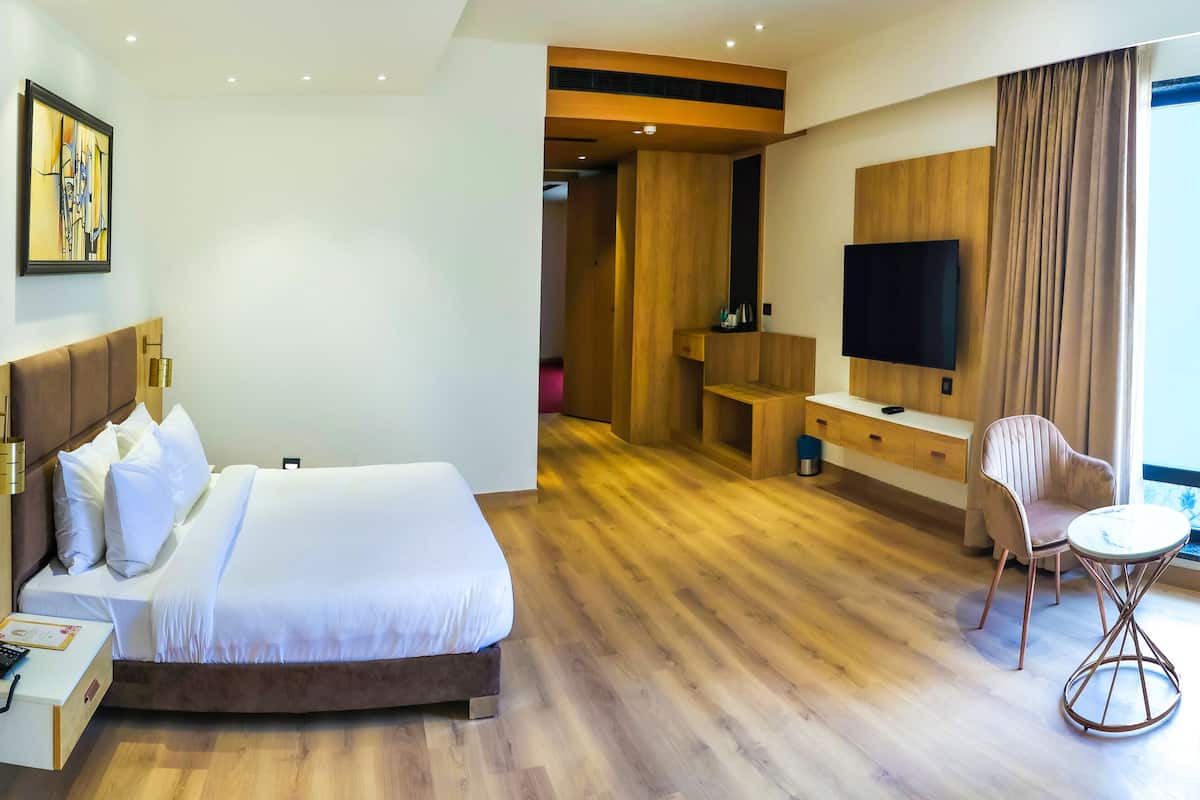 A hotel room with a bed, bedside table, lamp, TV, and a seating area with chairs and a table.