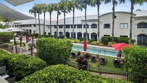 Un resort con piscina, palmeras y un edificio blanco con ventanas arqueadas.