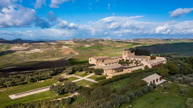 A large, historic building with multiple wings and a central courtyard, surrounded by lush green fields and trees. - Principi di Butera 14 (Butera)
