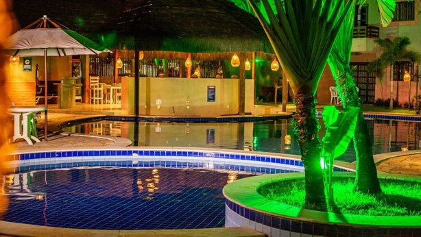 A nighttime pool area with a thatched-roof structure, a small pool, and a palm tree.