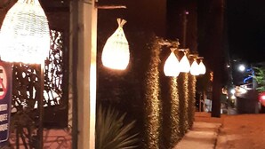 A nighttime street view with a building featuring a decorative metal fence and hanging light fixtures.