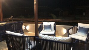 A balcony with wicker chairs and cushions, a wooden railing, and a view of the night sky.