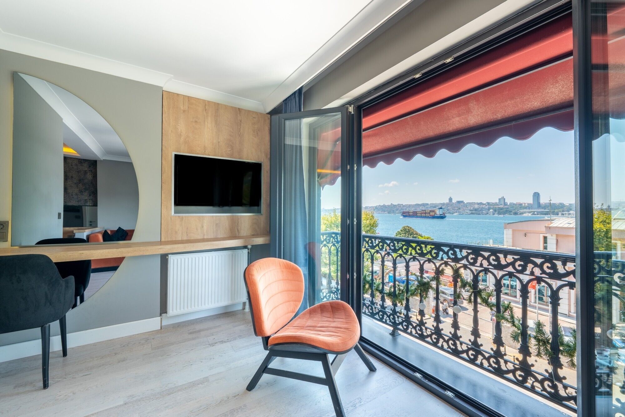 A modern interior with a dining area, a kitchen, and a large window with a view of a body of water and a cityscape.