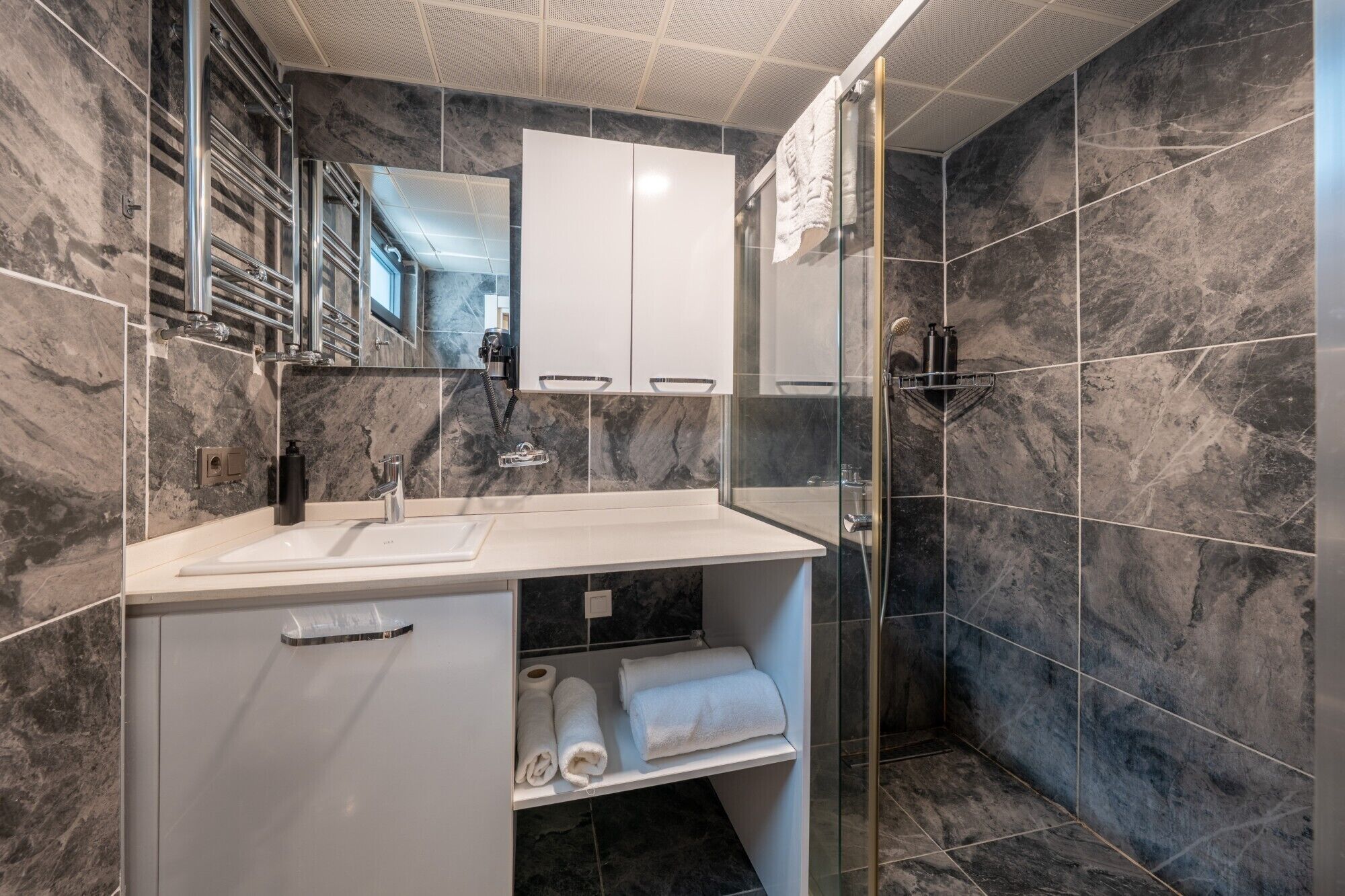 A modern bathroom with a marble backsplash, a white vanity with a sink, and a glass shower enclosure.