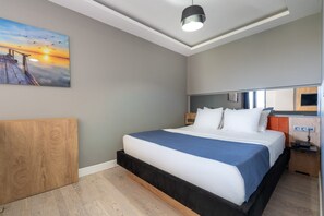Habitación de hotel con cama, cabecera de madera, un cuadro de un atardecer y una lámpara en el techo.