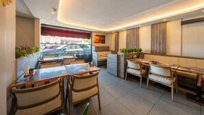 Ein Restaurantinnenraum mit verschiedenen Sitzgelegenheiten, darunter Tische und Sitzecken, Blick auf die Straße und einem modernen Design mit Holzelementen.