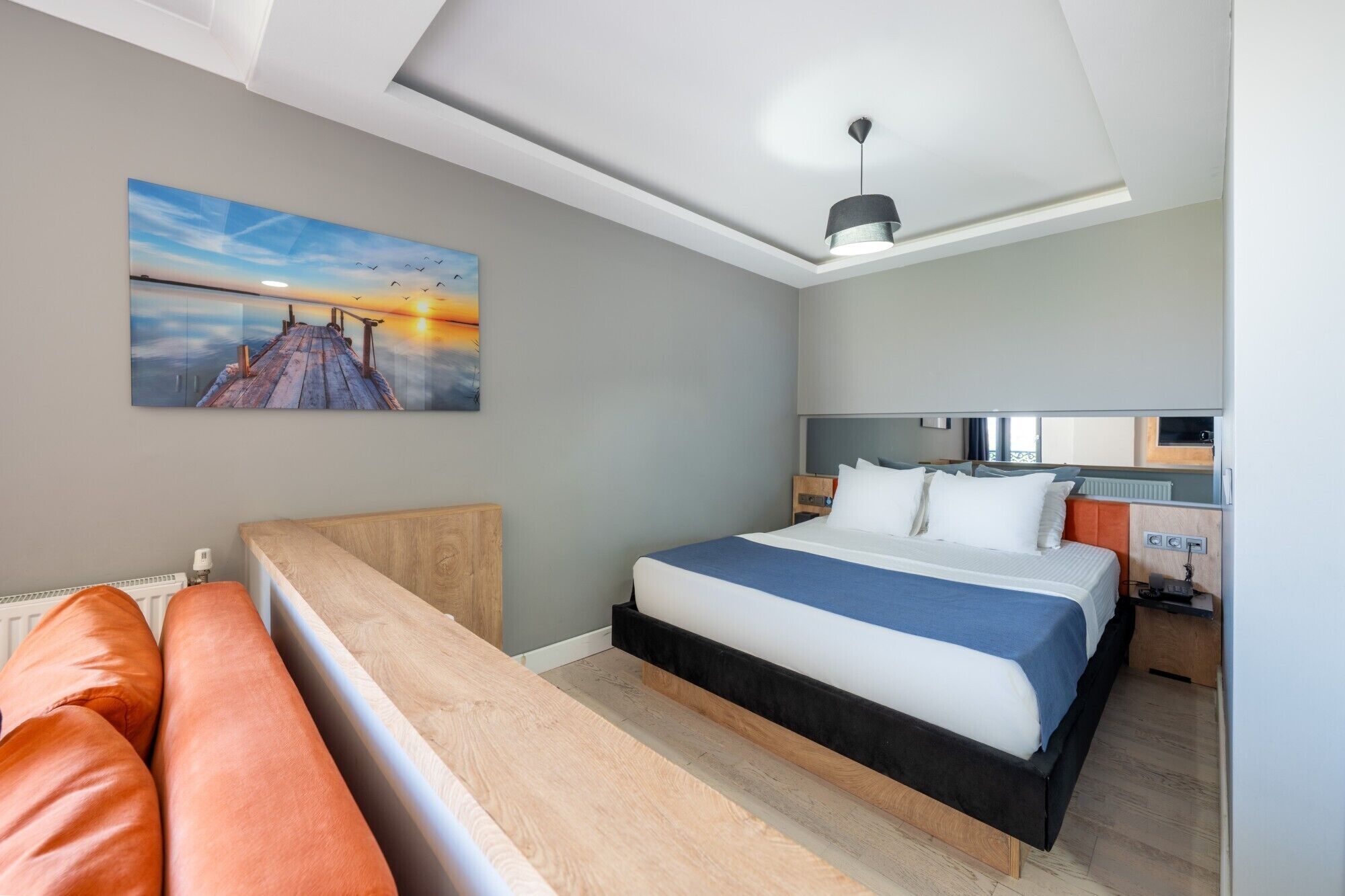 Una habitación de hotel moderna con cama, un banco, un cuadro y una lámpara en el techo.
