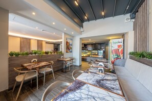 Un restaurante con mesas y sillas de mármol, una zona de cocina y un área de estar con vista a la ciudad.