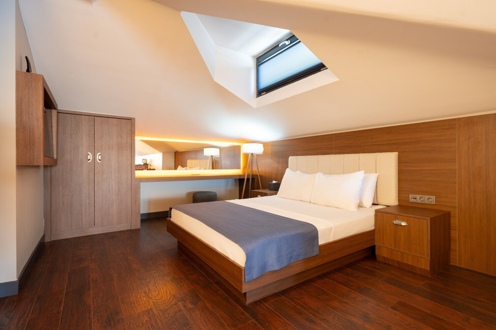 Ein modernes Hotelzimmer mit Oberlicht, einem Bett, einem Schreibtisch und einem Kleiderschrank.