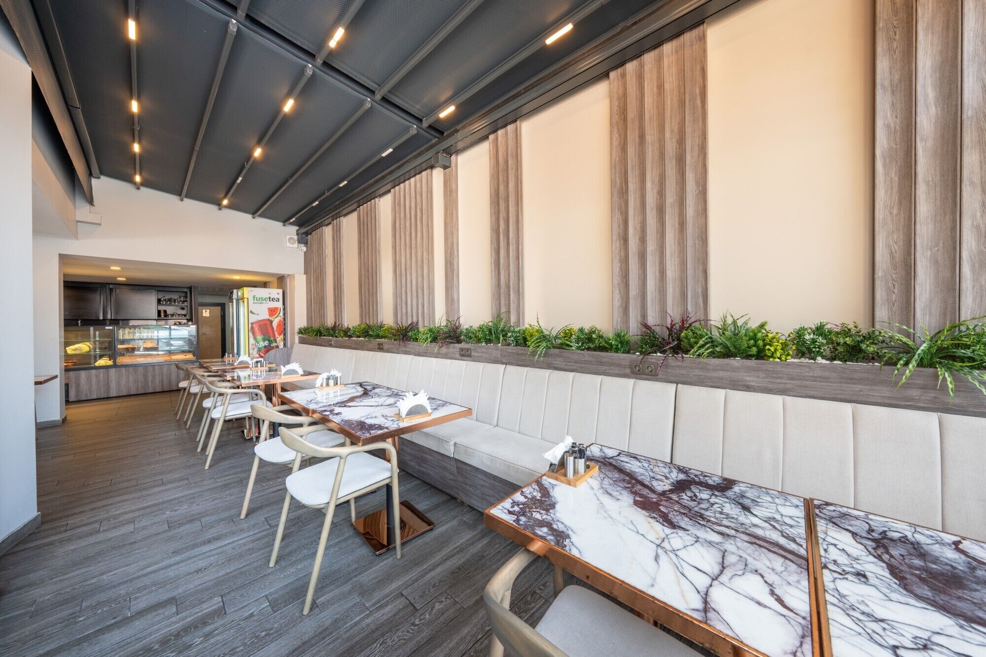 Un restaurante con mesas y sillas de tapa de mármol, una barra con una vitrina y una pared con persianas verticales.