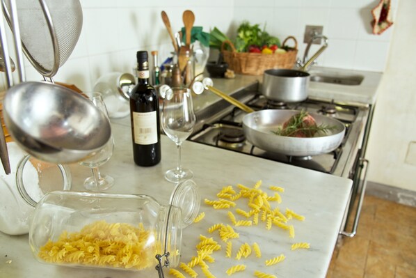 Una cocina con estufa, ollas, una botella de vino, copas y pasta.