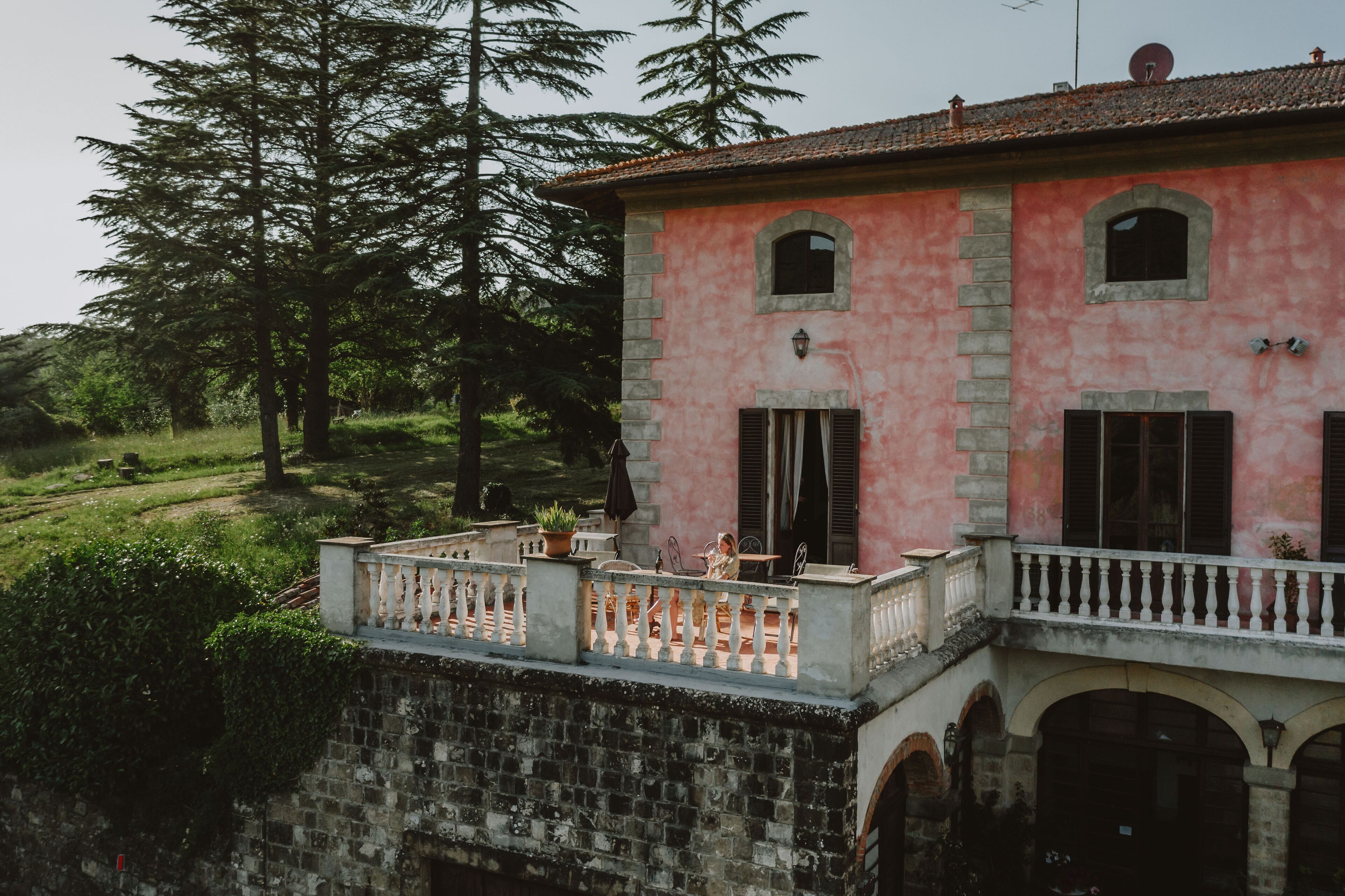Un bâtiment rose doté d’un balcon, de murs en pierre et d’un jardin.