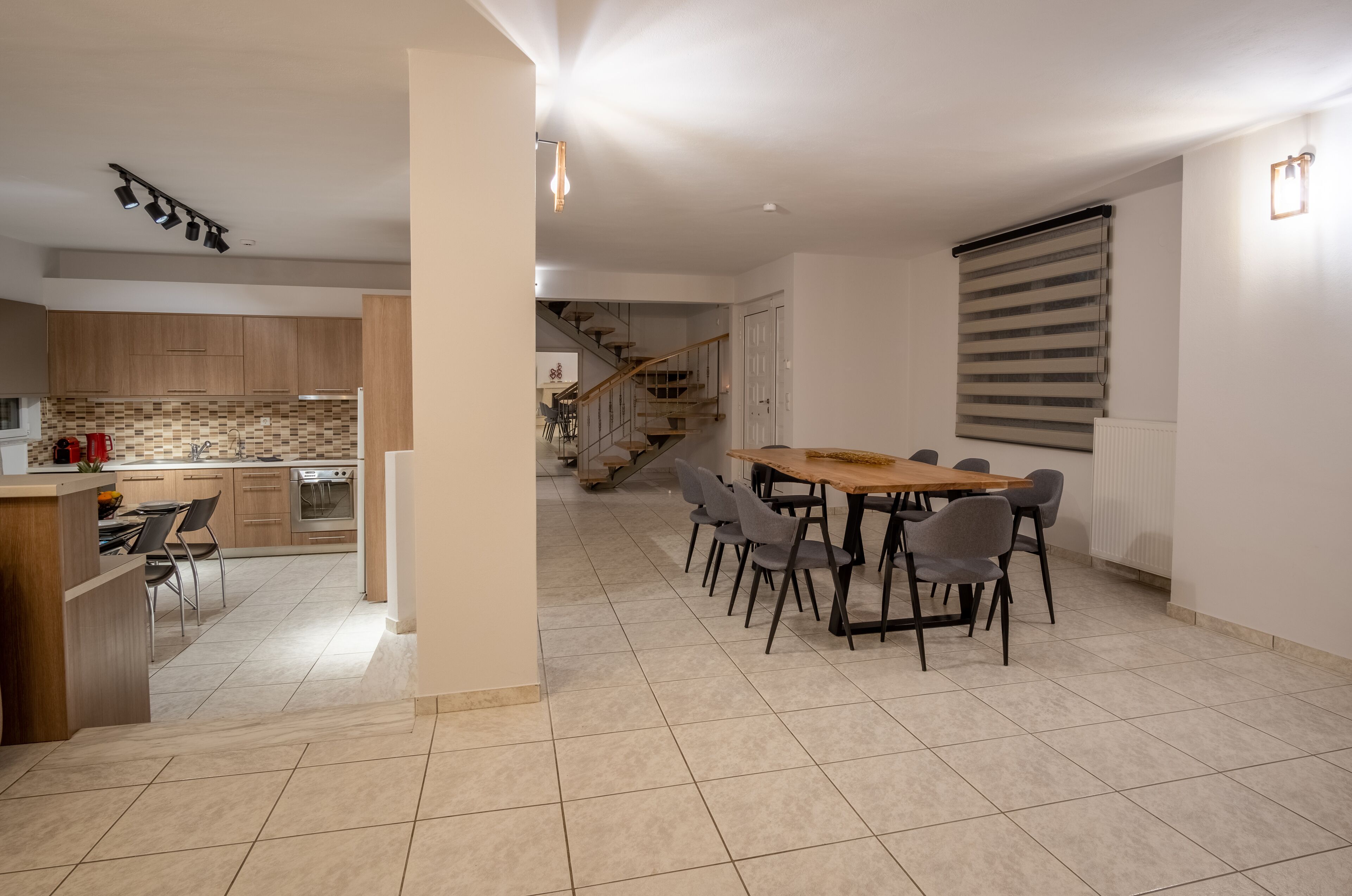 A modern kitchen with wooden cabinets, a dining area with a wooden table and chairs, and a staircase leading to another level.