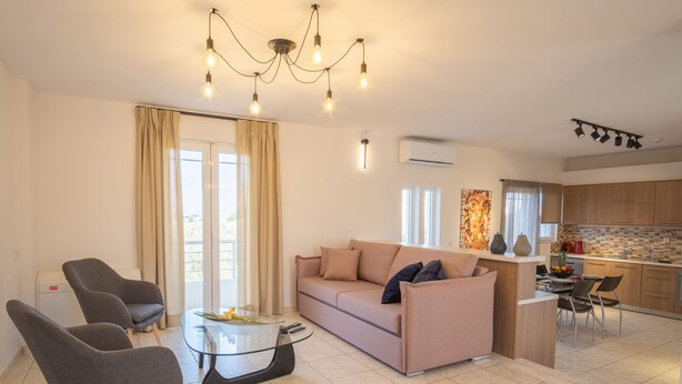 A modern living room with a sofa, two armchairs, a glass coffee table, and a kitchen area with a dining table and chairs. - Villa Cool with Private Pool (Malevizi)