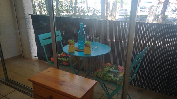 A small balcony with a round table, chairs, and a wooden cabinet.
