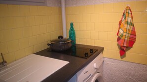 A kitchen with yellow tiles, a stove, a sink, and a washing machine.