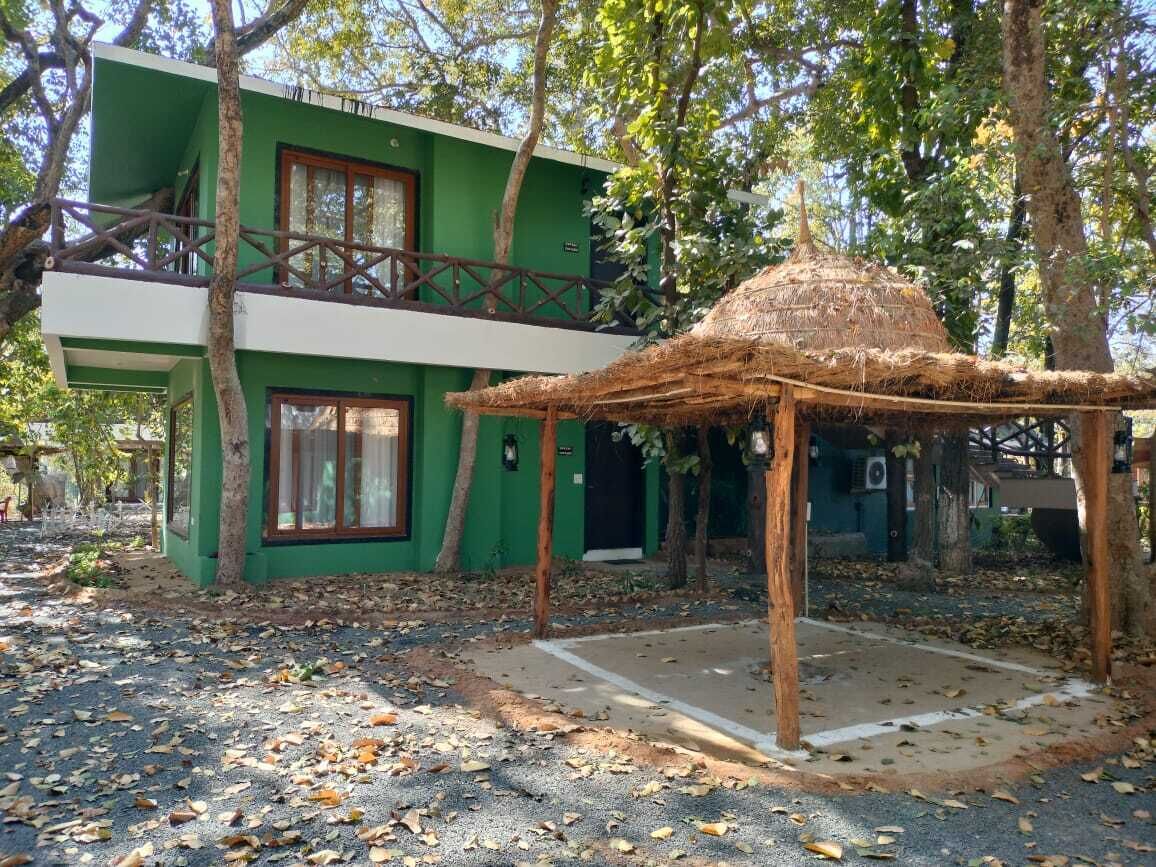 A two-story building with a green exterior and a thatched-roof structure in front.