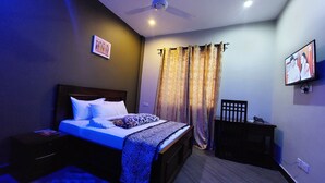 Ein Schlafzimmer mit Bett, Nachttisch, Sessel, Fernseher und Deckenventilator.