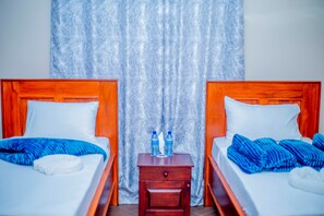 Una habitación de hotel con dos camas, una mesita de noche de madera y una cortina.