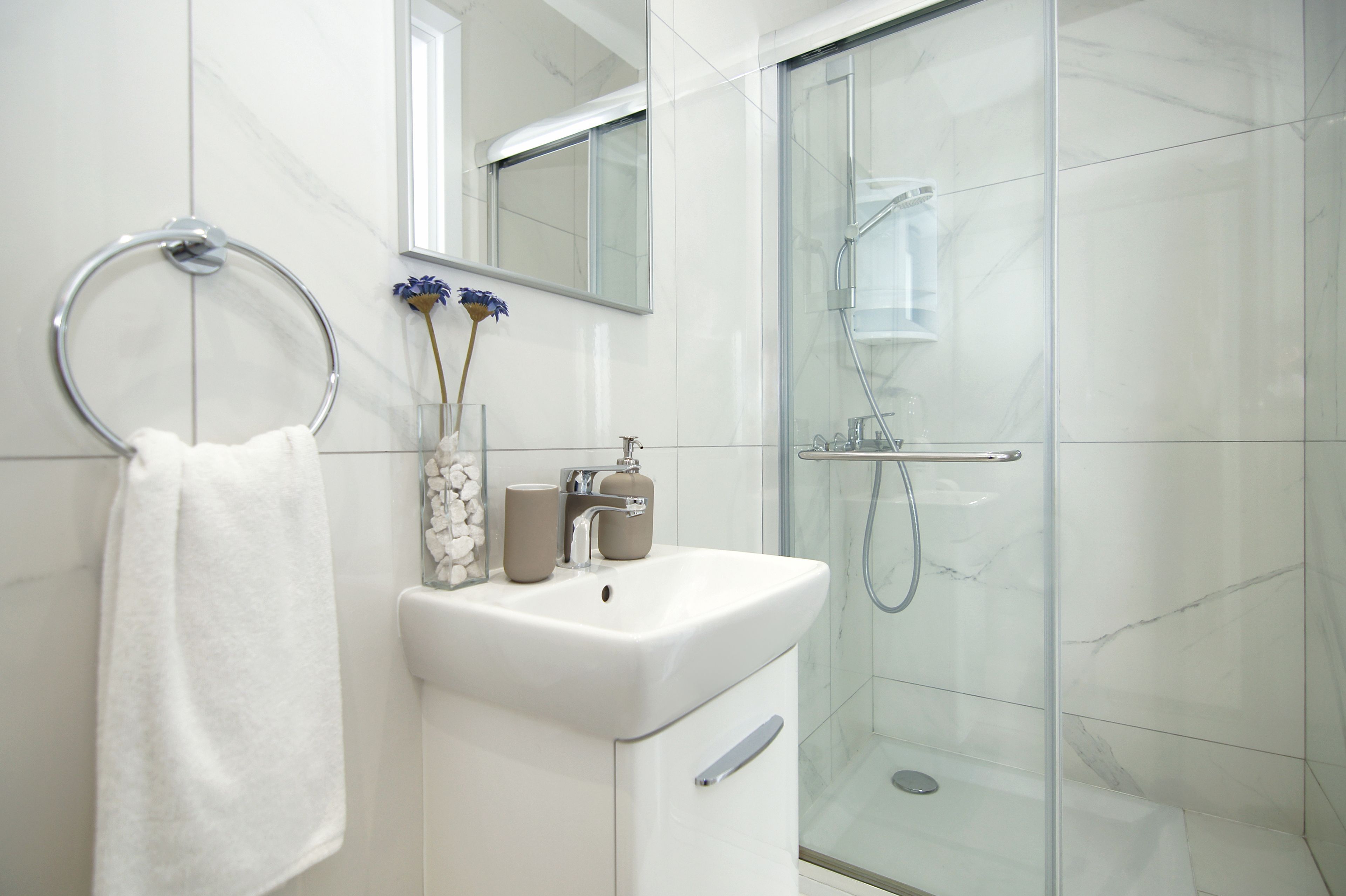 A modern bathroom with a glass shower enclosure, a white sink, and a towel ring with a single towel.