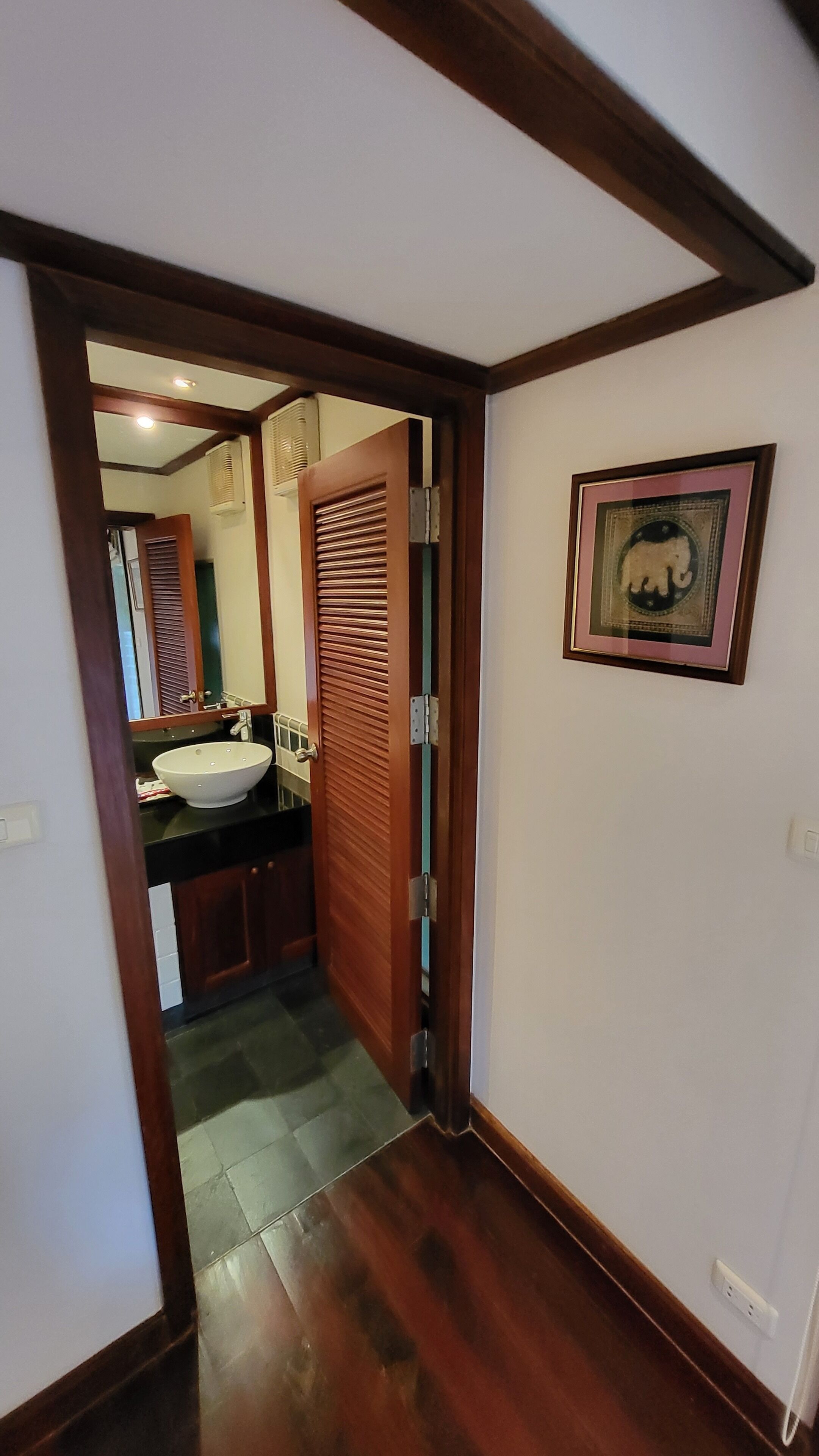 A hallway with a wooden door leading to a bathroom with a sink and mirror.