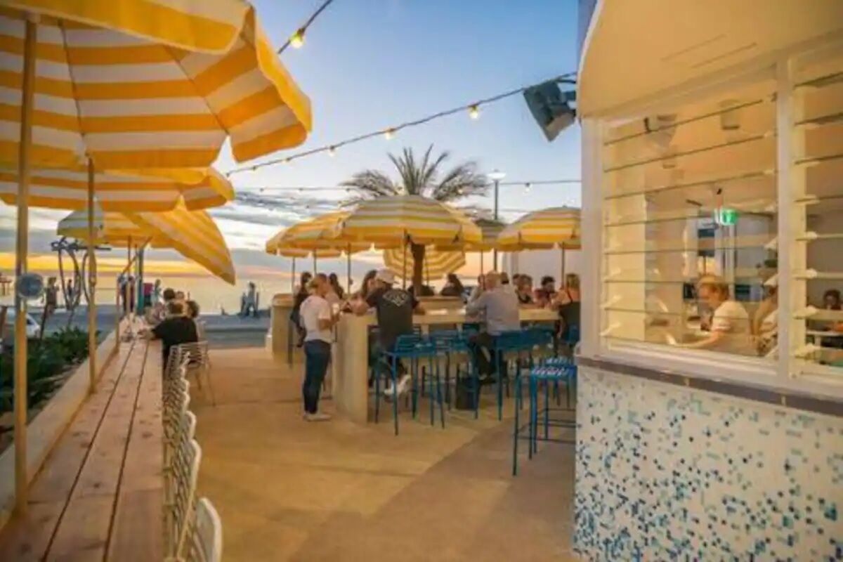 An outdoor seating area with striped umbrellas and tables, overlooking a body of water.