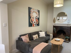 A living room with a grey sofa, a wooden coffee table, a fireplace, and a painting on the wall. - Beach Hideaway At Henley (Henley Beach)