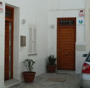A white building with a wooden door, a window with shutters, and two potted plants. - APARTMENT IN MONACHIL PUEBLO/GRANADA (ANDALUCIA) (Monachil)
