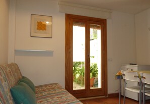 A small room with a sofa, a table, a chair, a door leading to a balcony, and a refrigerator. - APARTMENT IN MONACHIL PUEBLO/GRANADA (ANDALUCIA) (Monachil)