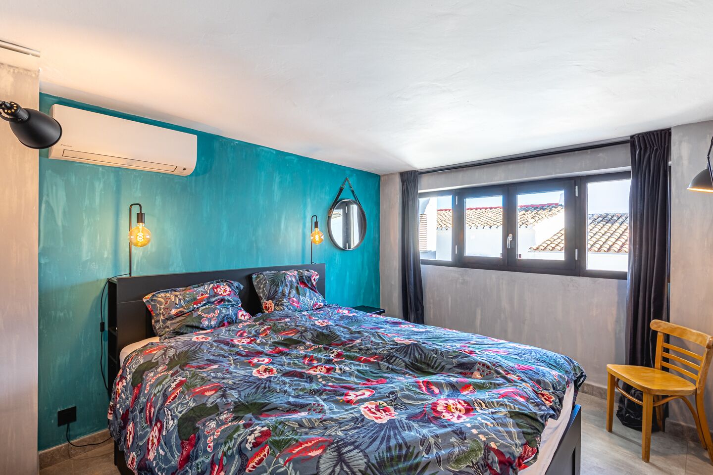 A bedroom with a bed, a chair, a window, and a wall-mounted air conditioner.