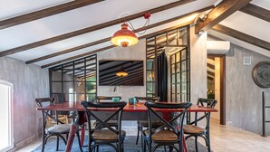 A dining area with a wooden table and chairs, a red pendant light, and a view of a kitchen through a glass door.
