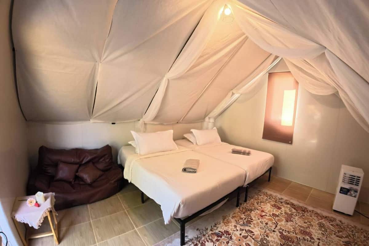 Ein gemütliches Zelt-ähnliches Zimmer mit einem Bett, Kissen, einem kleinen Tisch mit Kerze und einem Heizgerät.