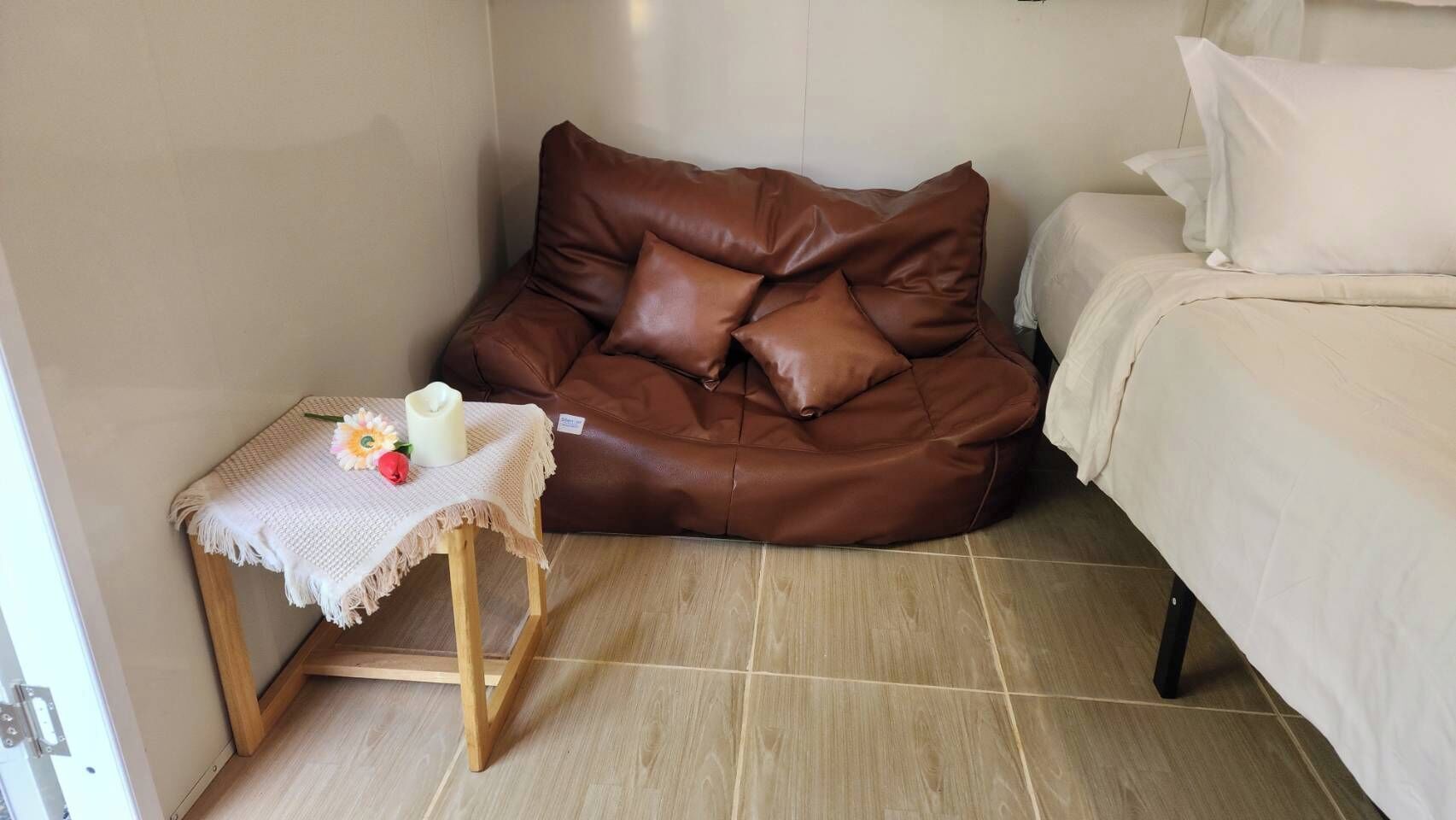 Et værelse med en brun lædersofa, et lille træbord med hvid dug og en seng med hvide sengetøj.