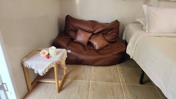A room with a brown leather couch, a small wooden table with a white tablecloth, and a bed with white bedding.