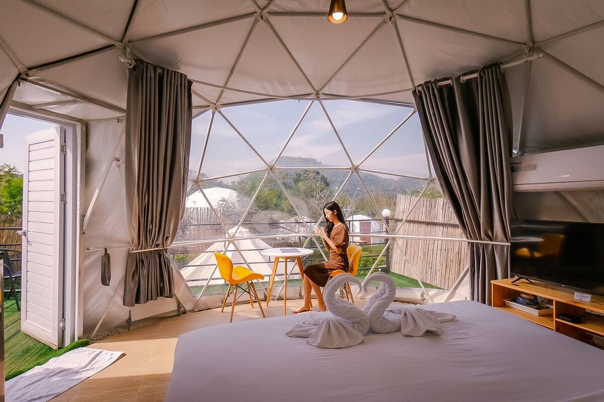 Ein Zelttyp-Zimmer mit Bett, Fernseher, Vorhängen, Tisch und Stuhl.