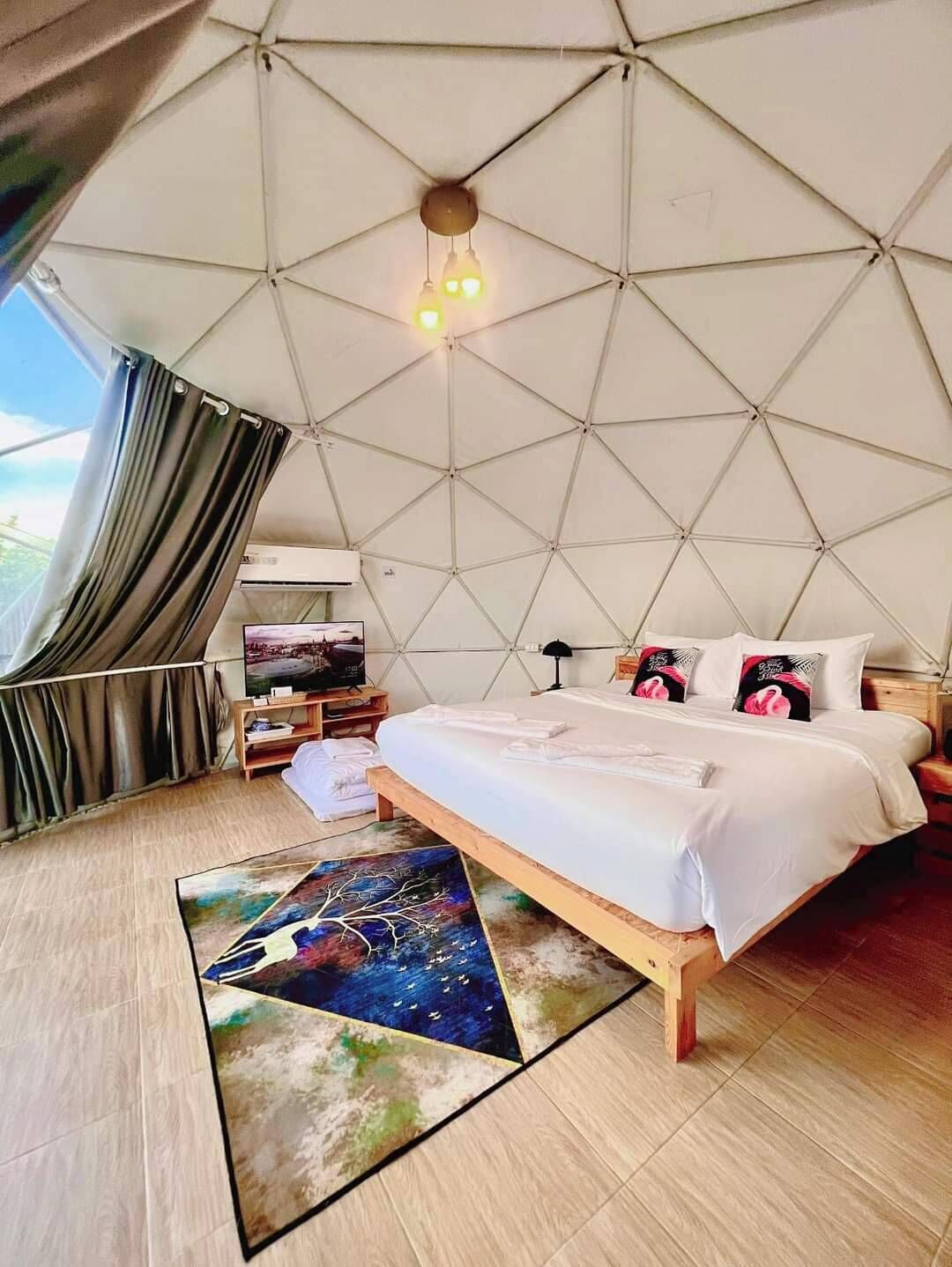 A spacious tent-style room with a bed, a flat-screen TV, and a view of the outdoors.