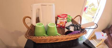 A wicker basket with green cups, a white mug, a box of snacks, and a small table with a laptop.