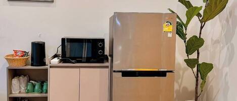 A kitchen with a stainless steel refrigerator, a microwave, and a shelf with kitchen items.