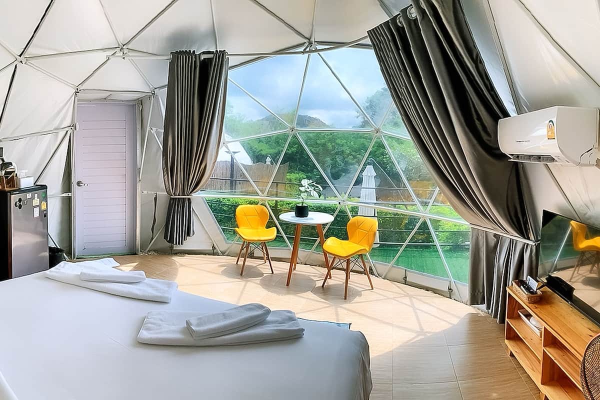 Ein Zeltraum mit Bett, kleinem Tisch und zwei gelben Stühlen, mit Blick auf Grün.