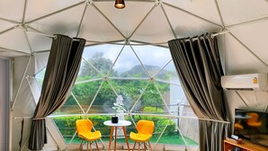 A tented room with a table and two chairs, a TV, and a view of greenery outside. - Glamping Hill Khaoyai (Pak Chong)