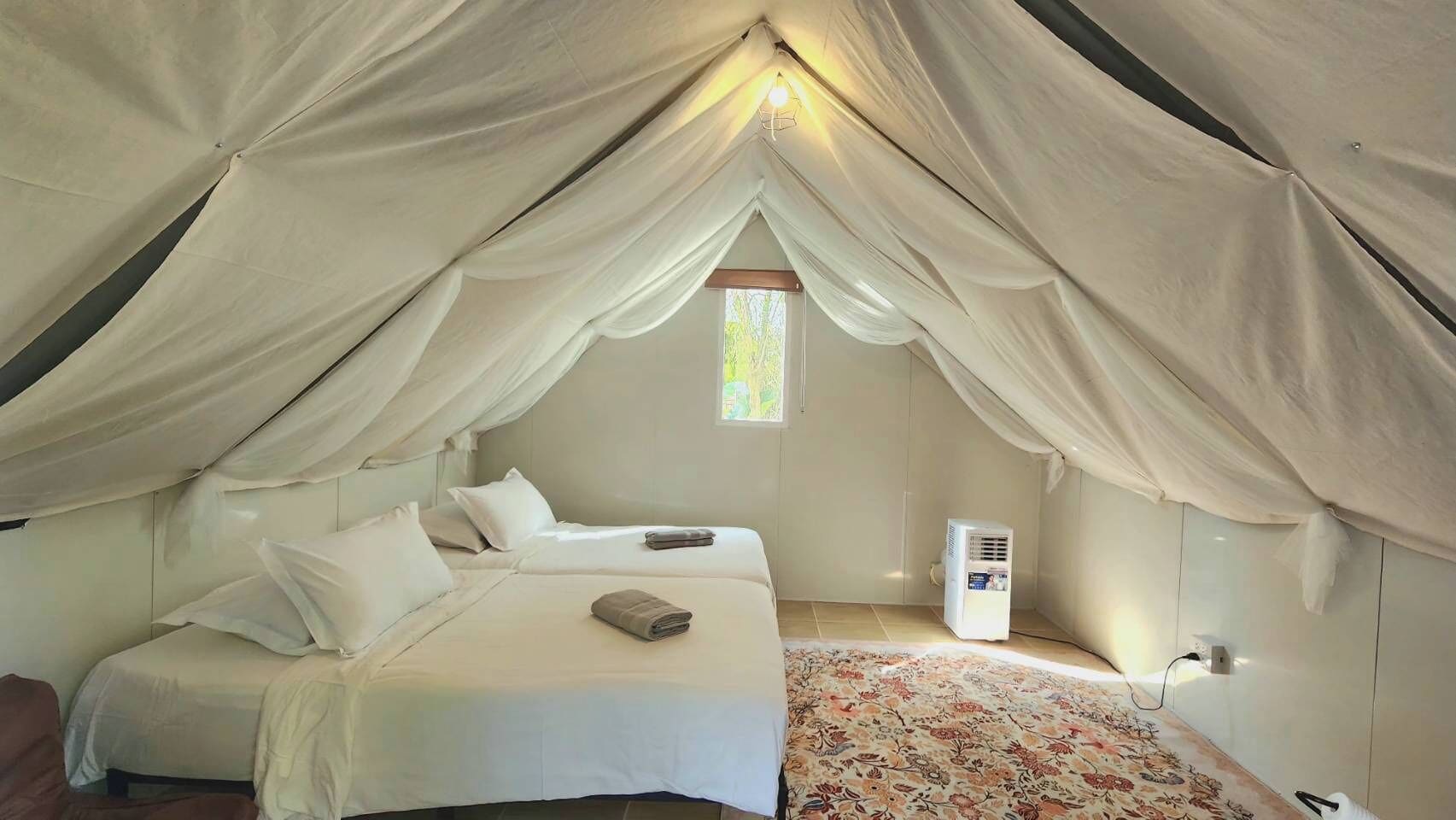 A tent-style room with two beds, a window, and a heater.