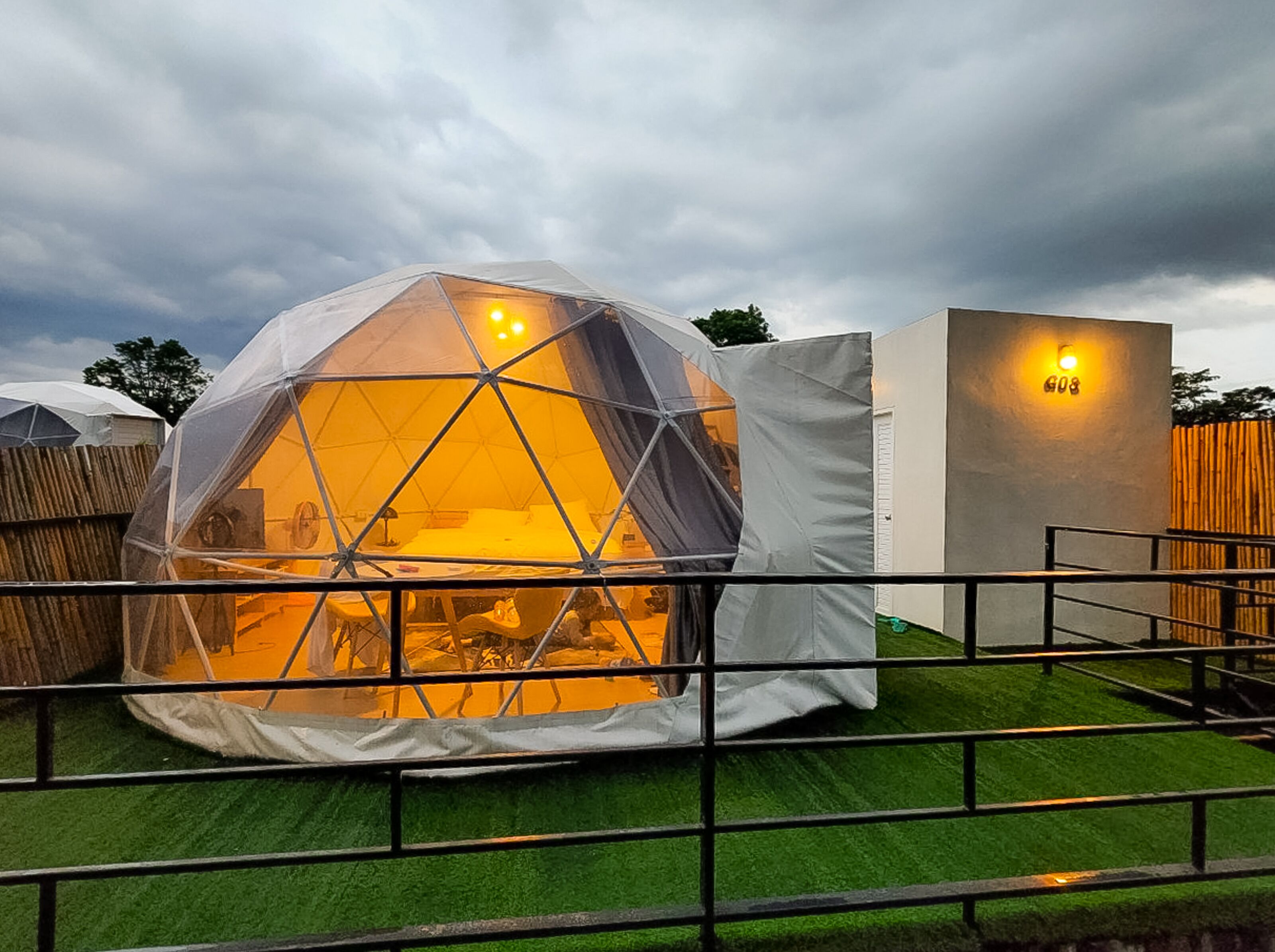 Estructura geodésica en forma de cúpula con interior visible, rodeada por una zona vallada con césped artificial.