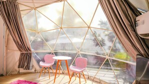 A geodesic dome room with a large window, two pink chairs, a small round table, and a pink rug. - Glamping Hill Khaoyai (Pak Chong)